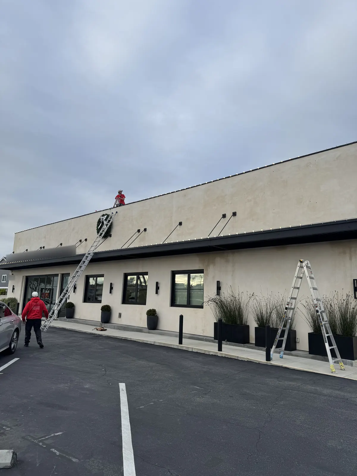 Crew on ladders and the roof installing lights on a commercial building in Corona del Mar