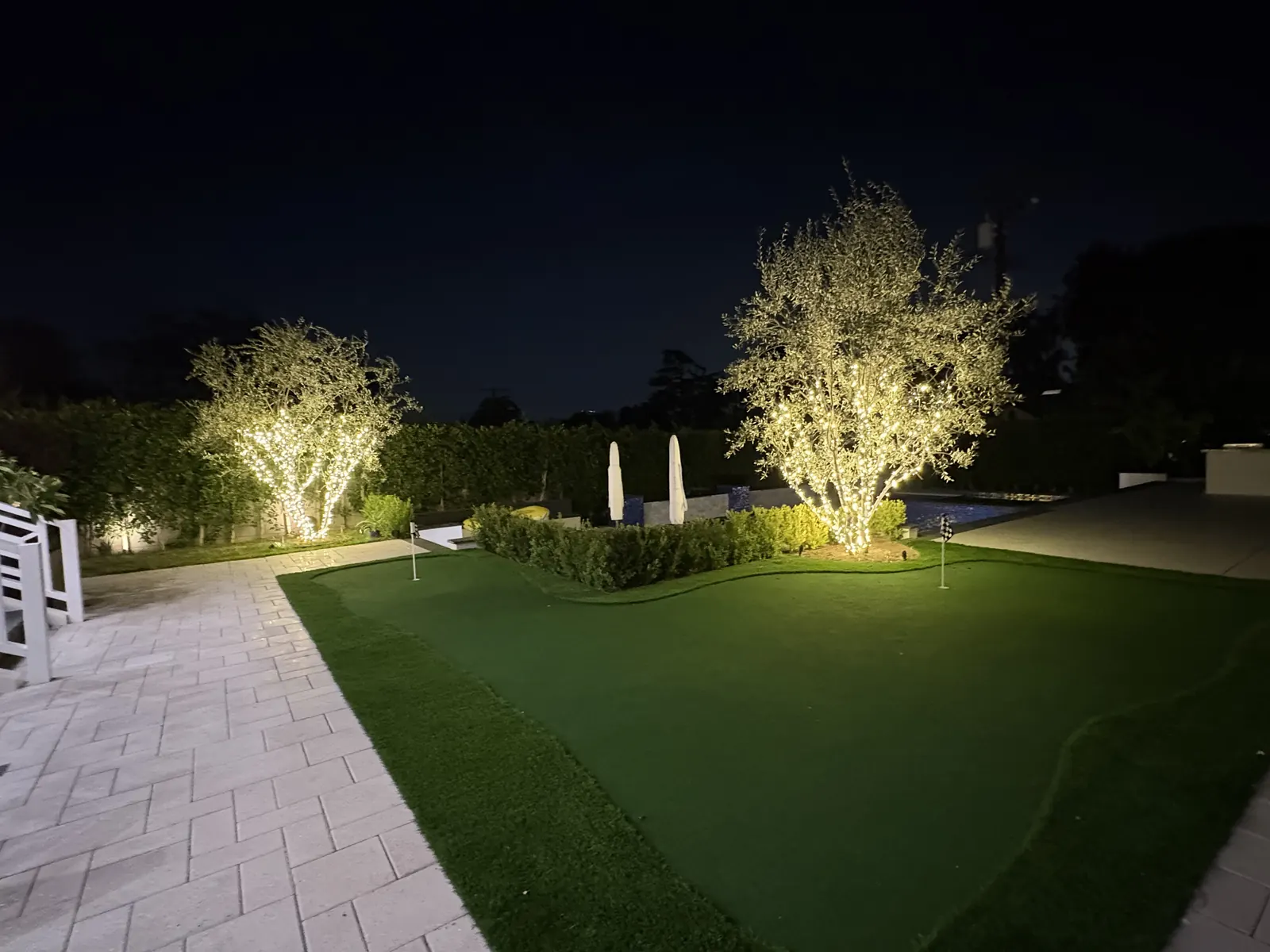 Backyard in Glendale with two trees wrapped in warm white lights beside a putting green