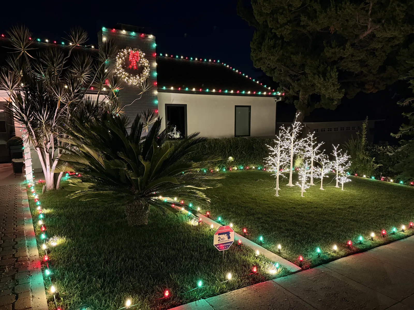 Home in Glendale with multicolor roofline and pathway lights, a lit wreath, and white light-up trees on the lawn