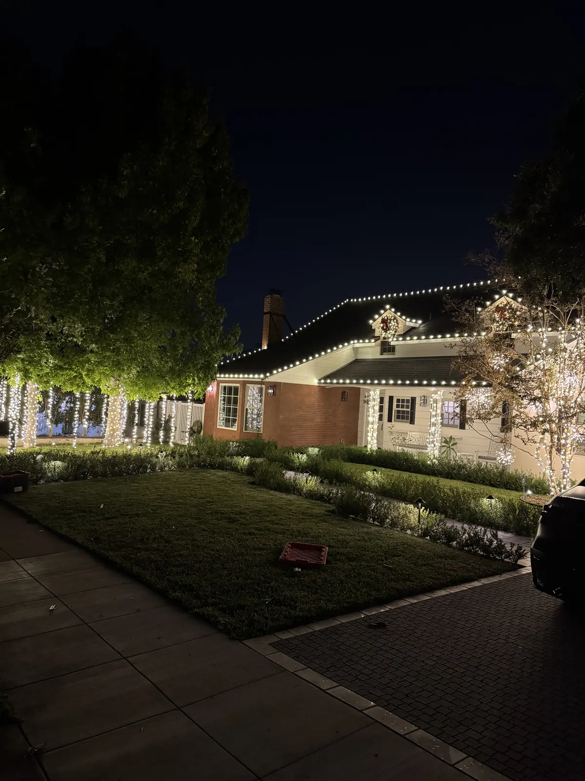 Home in Glendale with warm white roofline lights, light-wrapped tree trunks along the fence, and lit columns