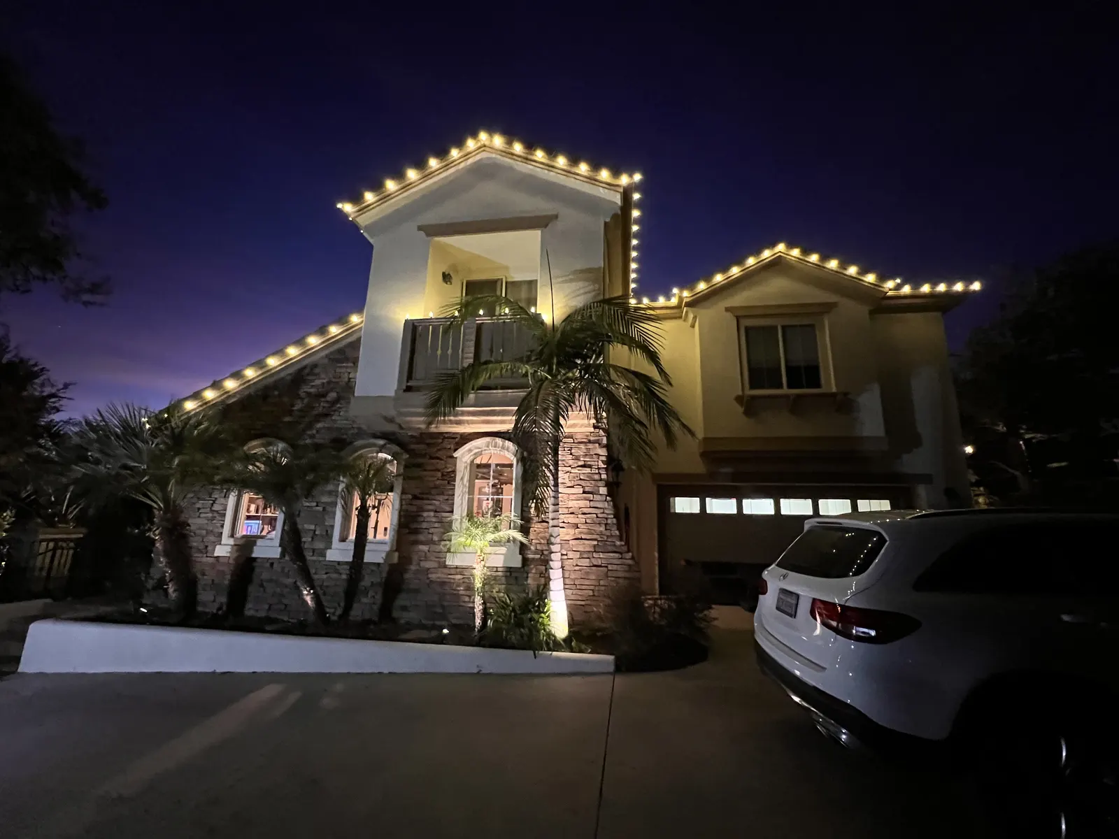 Spanish-style home with warm white roofline lights and a lit palm tree in the front yard