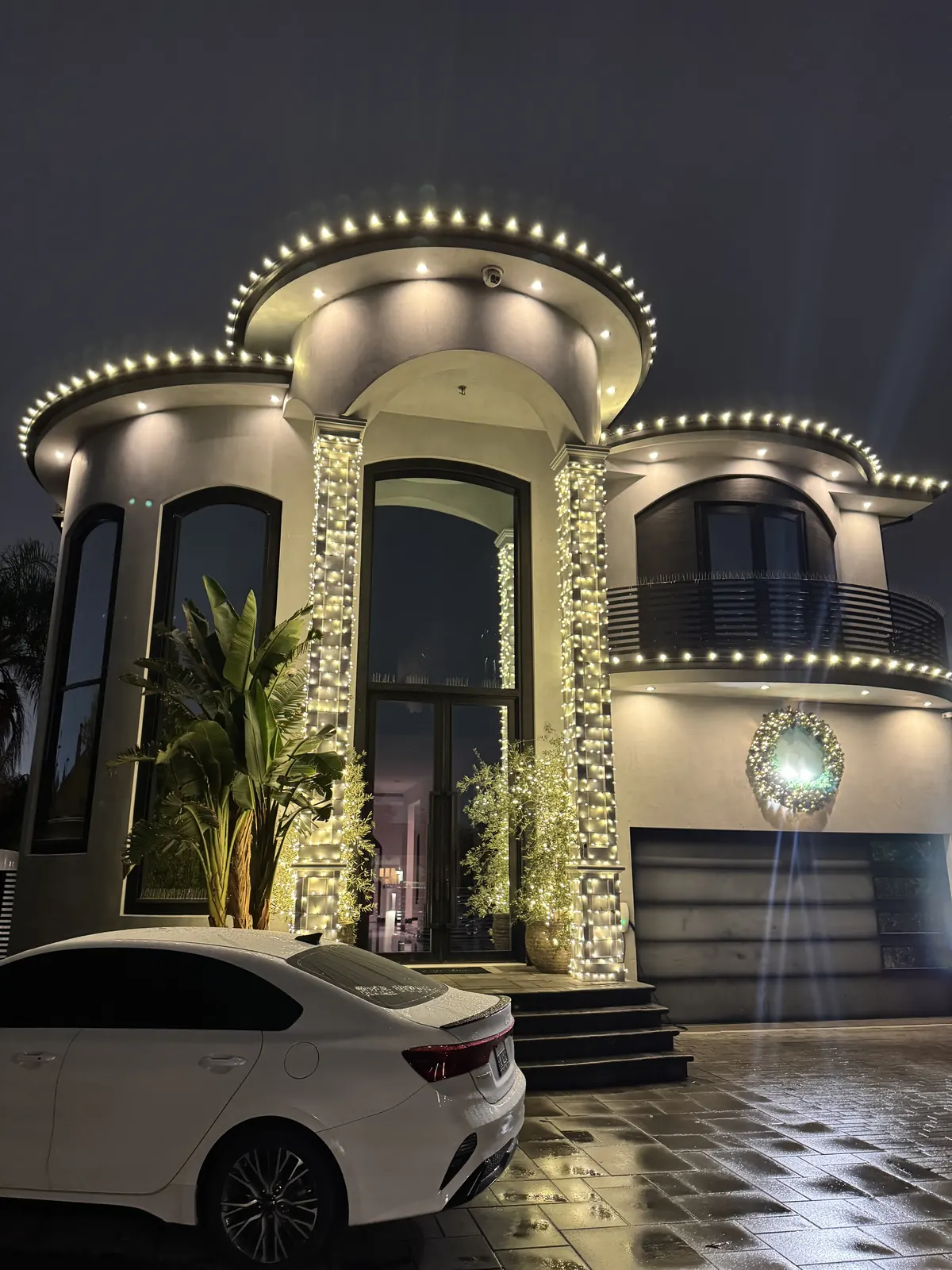 Modern home in North Hollywood with warm white lights on the curved rooflines, light-wrapped columns, and a lit wreath