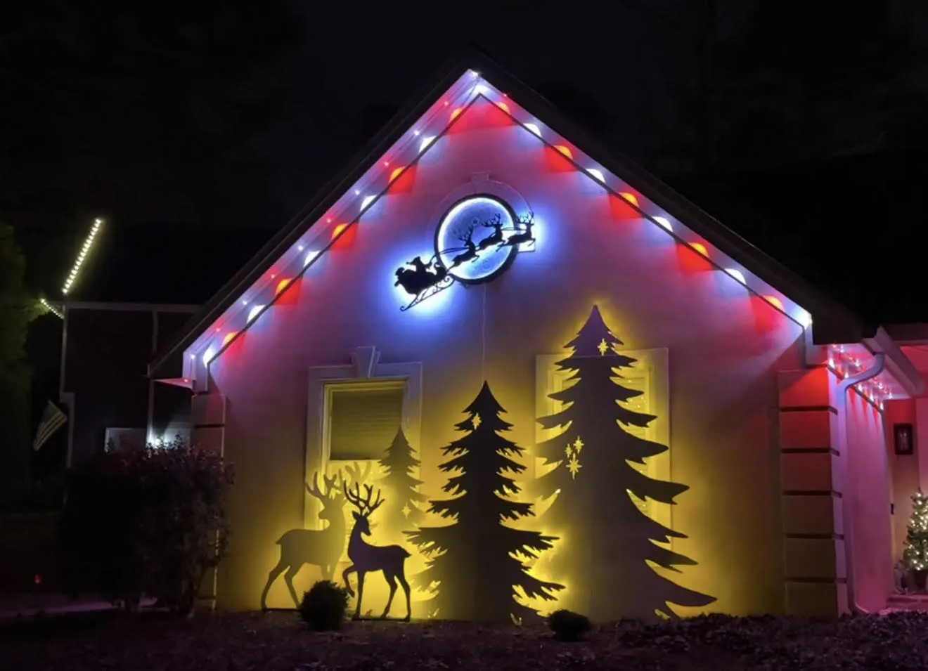 Permanent RGB roofline lighting in red and blue with a lit Santa sleigh and holiday tree silhouettes