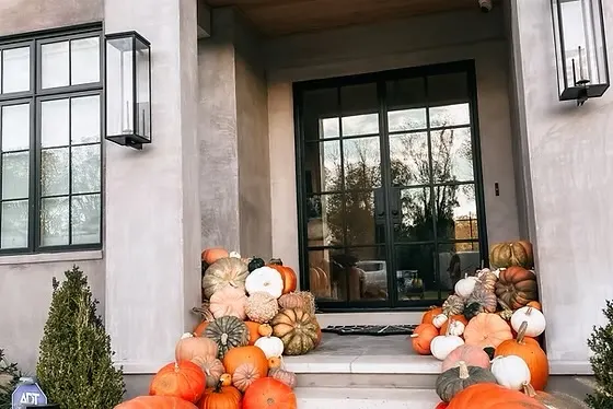 Mix of orange, green, and white pumpkins arranged around a modern home entryway