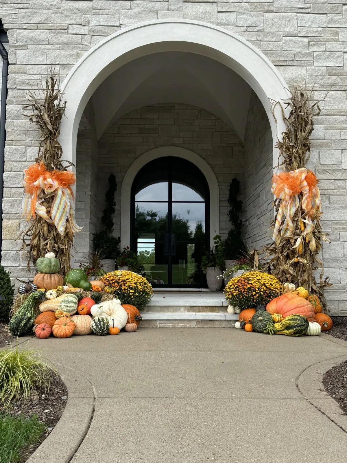 Stone arched entryway with corn stalk columns, mums, and a full heirloom pumpkin display