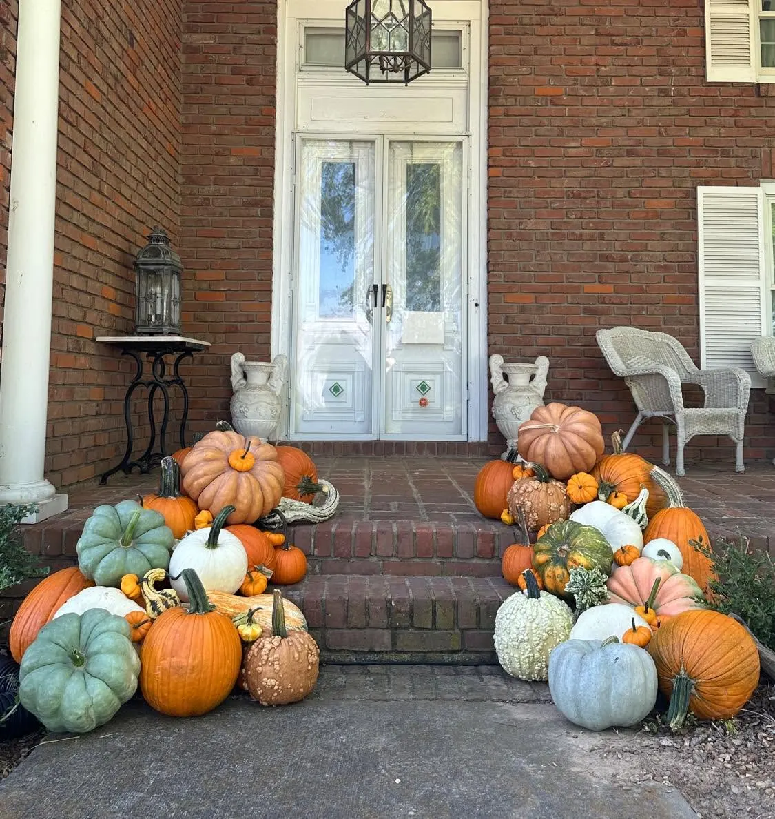 Brick home front porch with blue, orange, white, and specialty pumpkins grouped around French doors