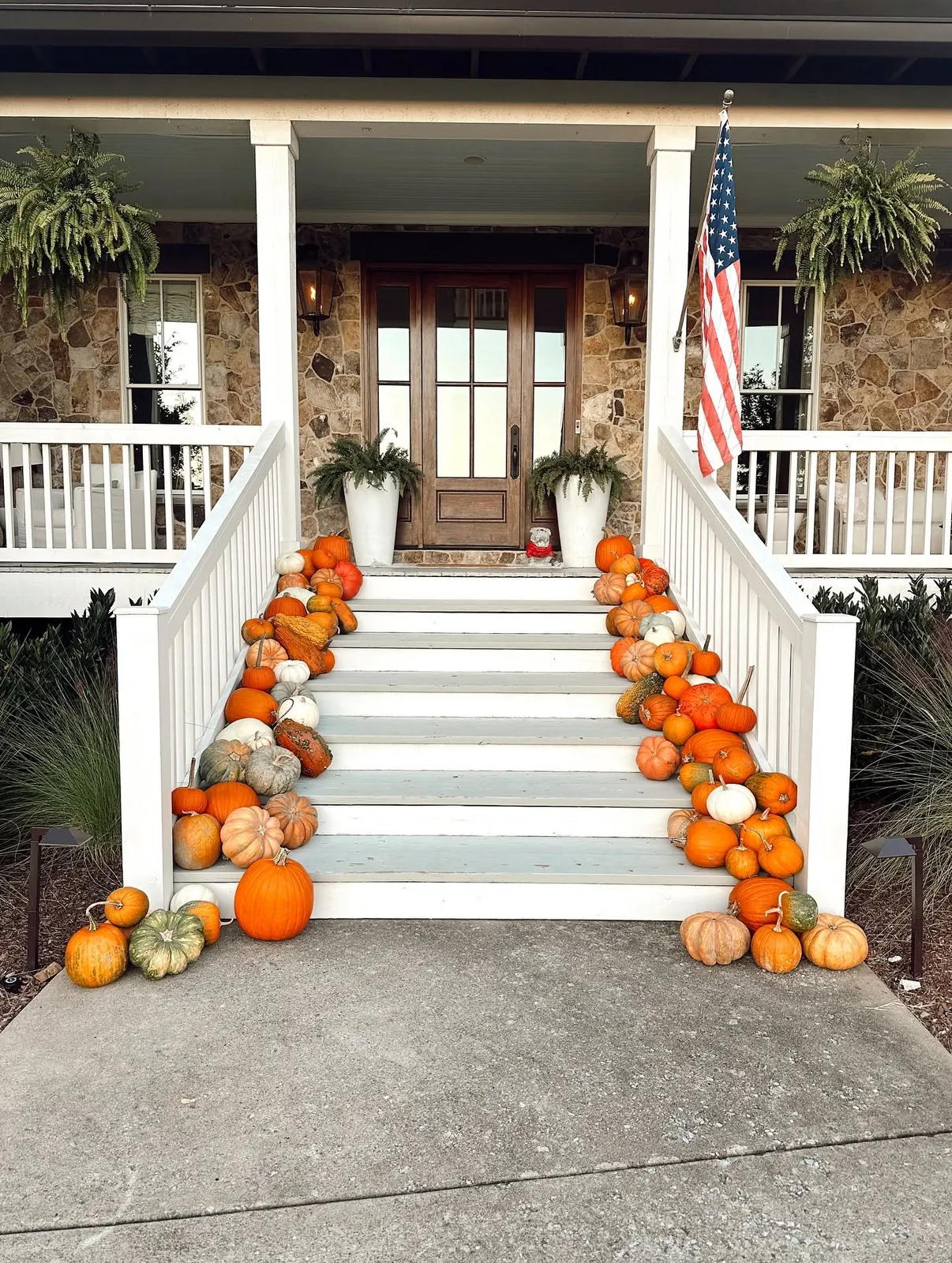 Heirloom and orange pumpkins lining both sides of white porch steps at a stone home