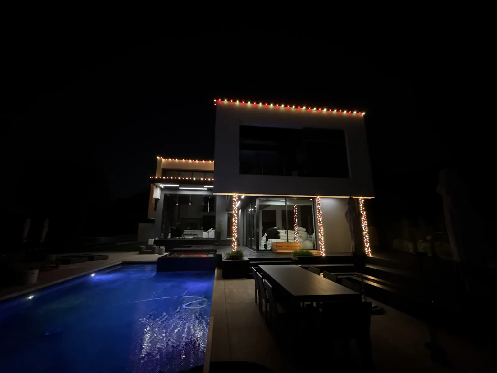 View across the pool to a modern home in Studio City with roofline lights and light-wrapped columns