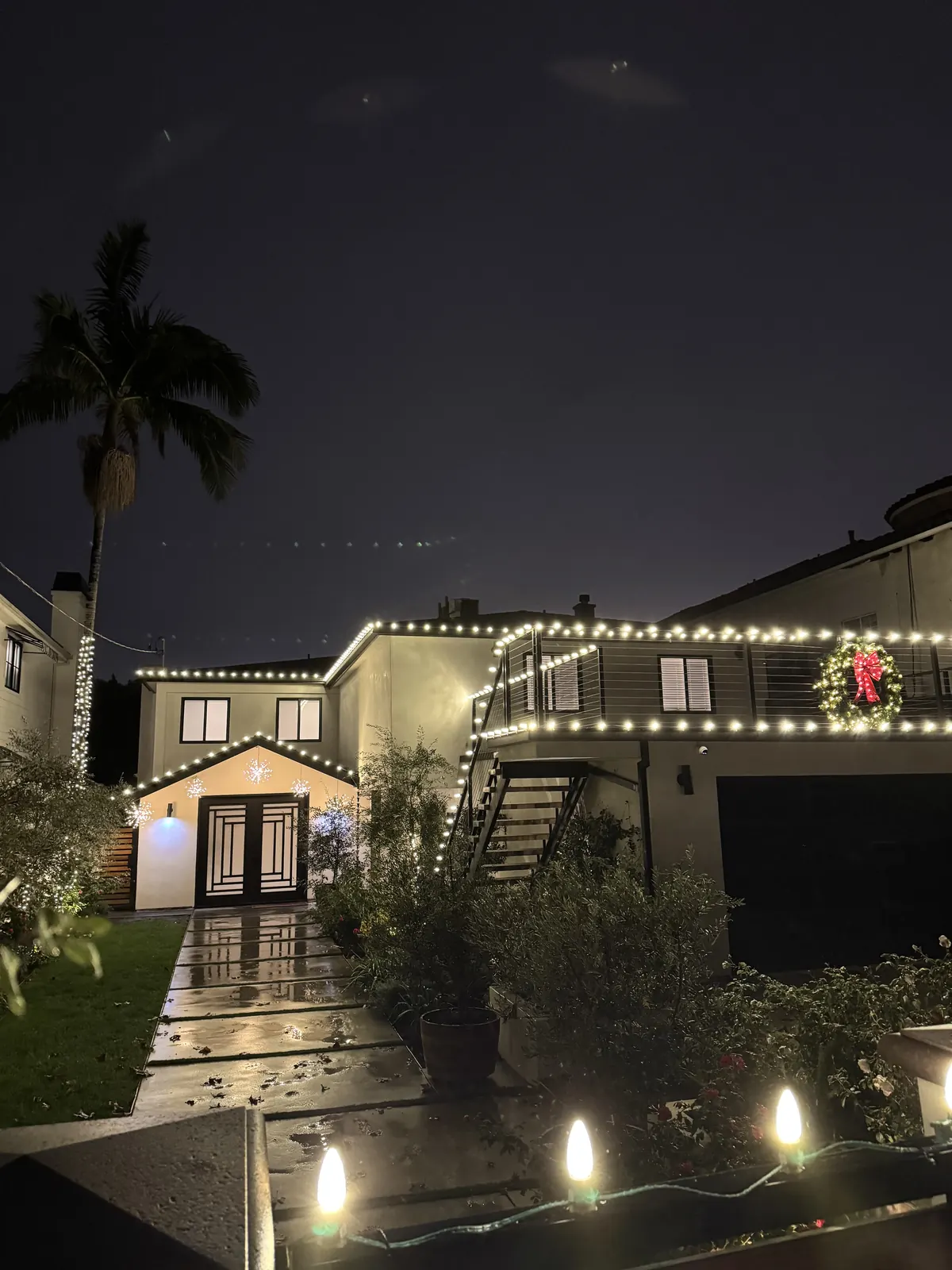 Home in Toluca Lake with warm white roofline and balcony lights, a lit wreath, and path lights along the walkway