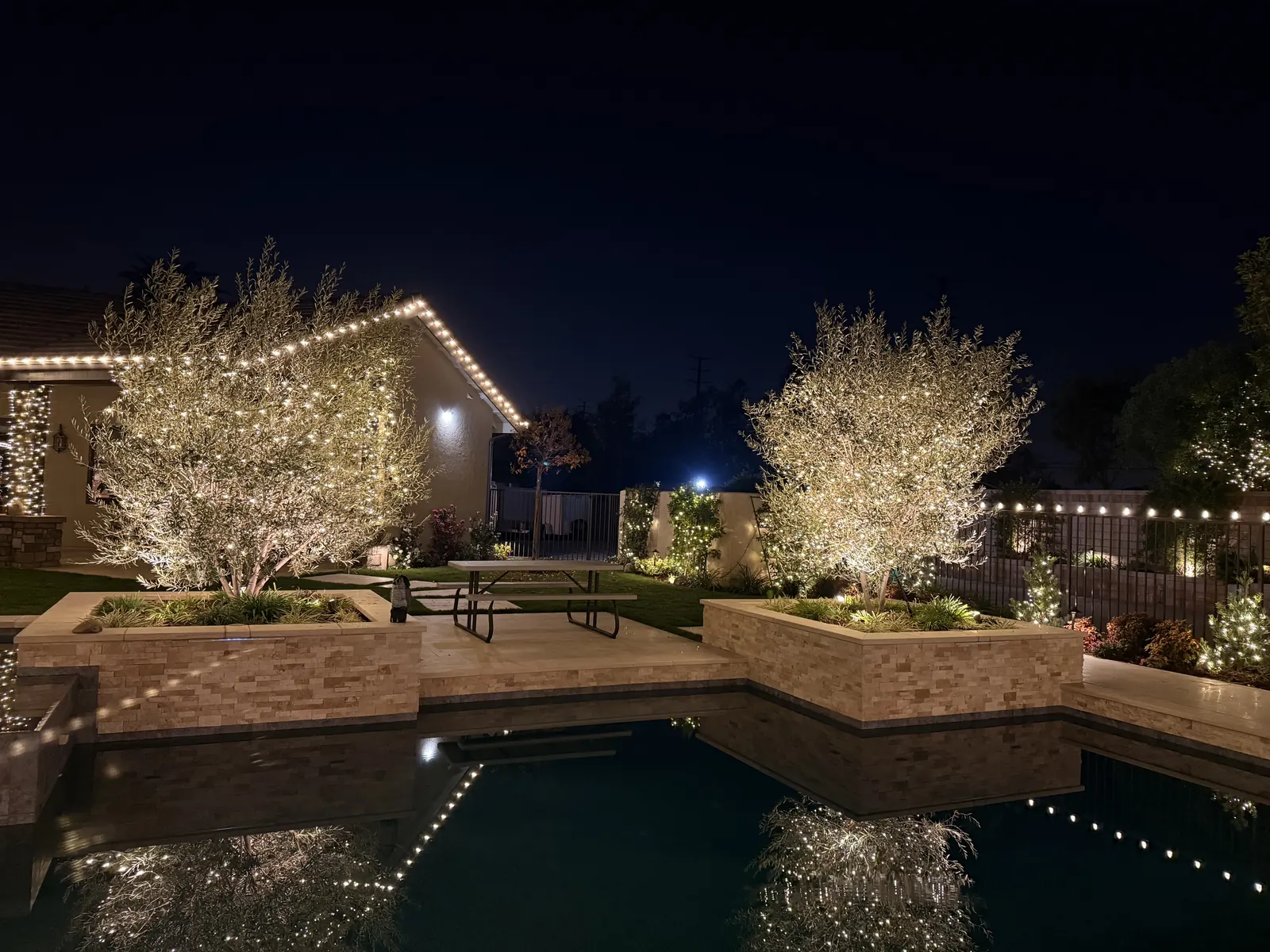 Backyard in Yorba Linda with light-wrapped trees and roofline lights reflected in the pool