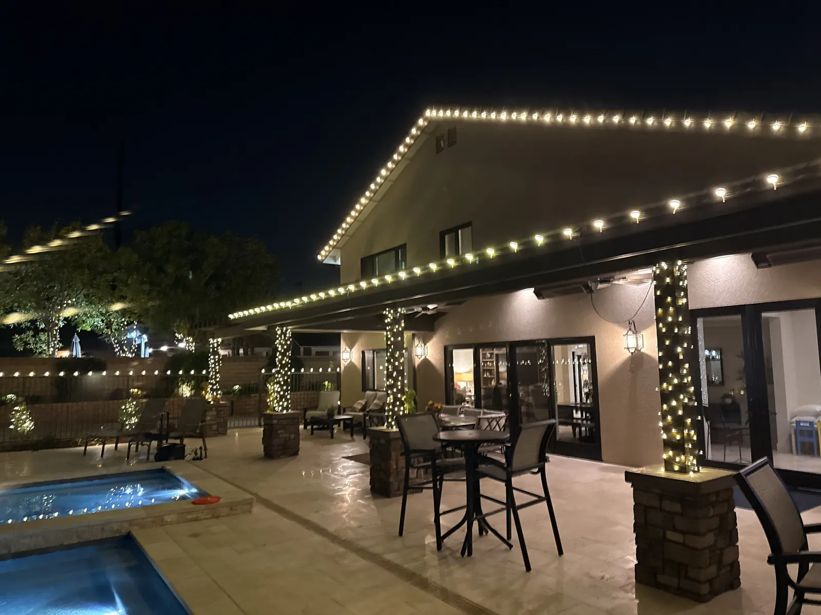 Back patio in Yorba Linda with roofline lights and light-wrapped stone columns beside the spa