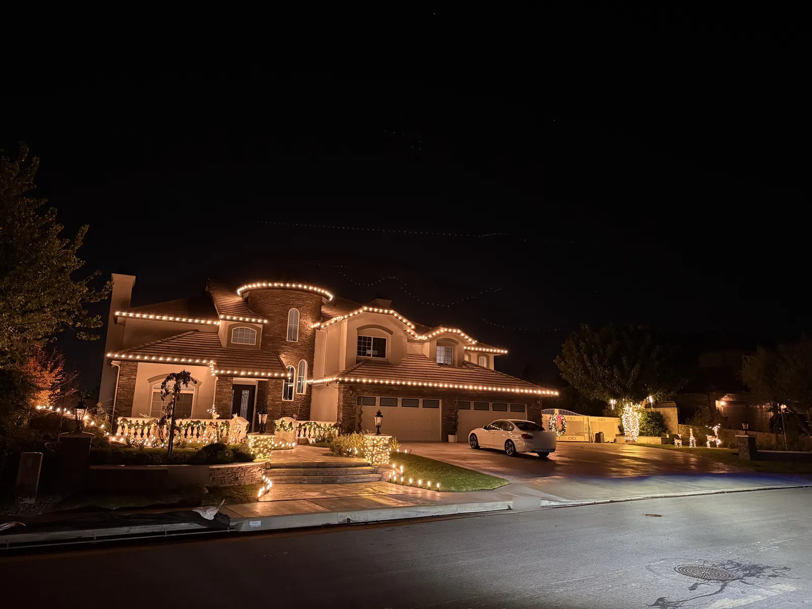 Two-story home in Yorba Linda with warm white lights on every roofline, lit stair railings, and light-wrapped trees